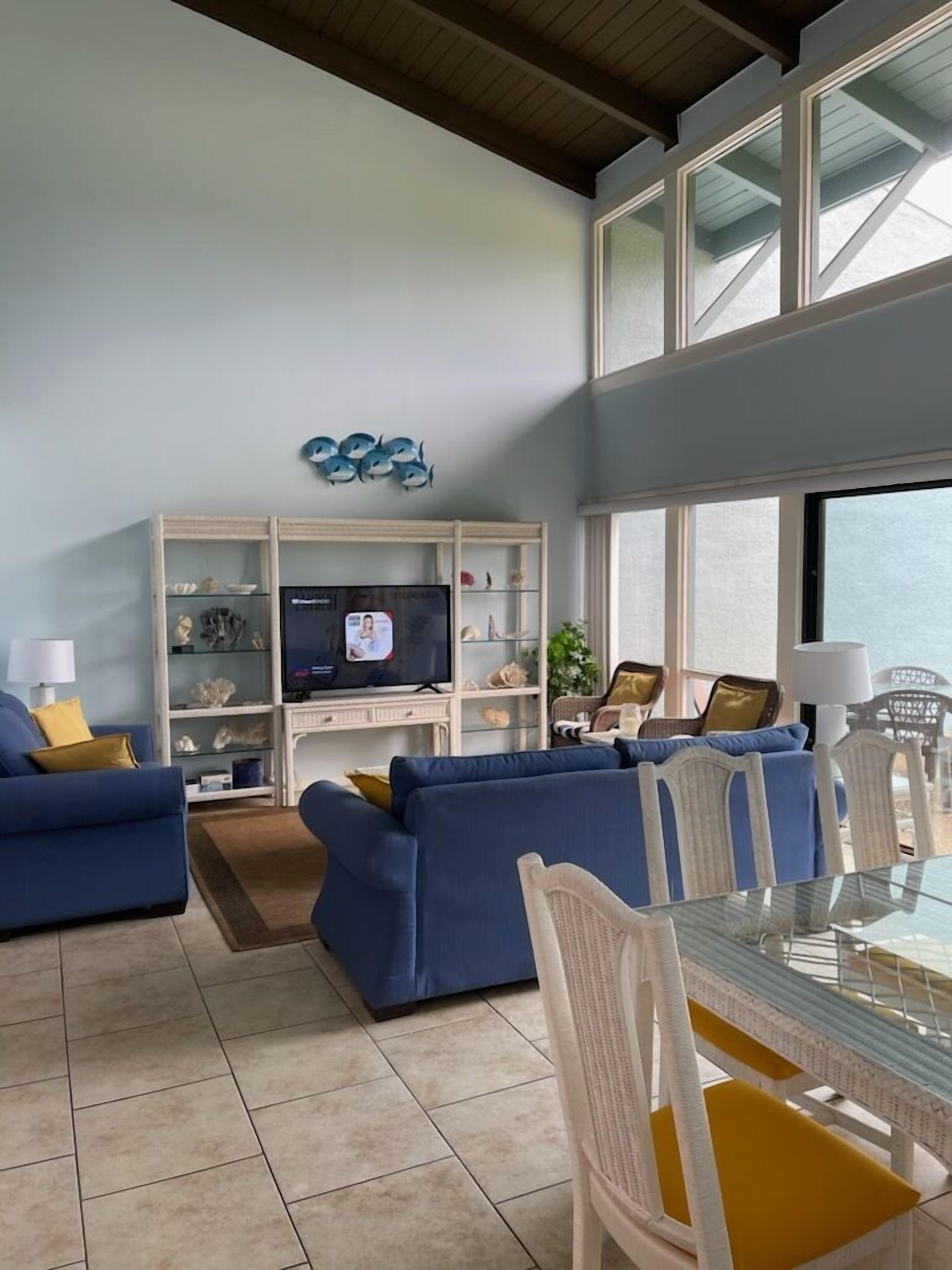A modern living room with a TV, blue sofas, a glass table, and a white chair.