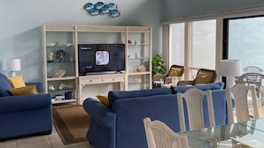 A modern living room with a TV, blue sofas, a glass table, and a white chair.