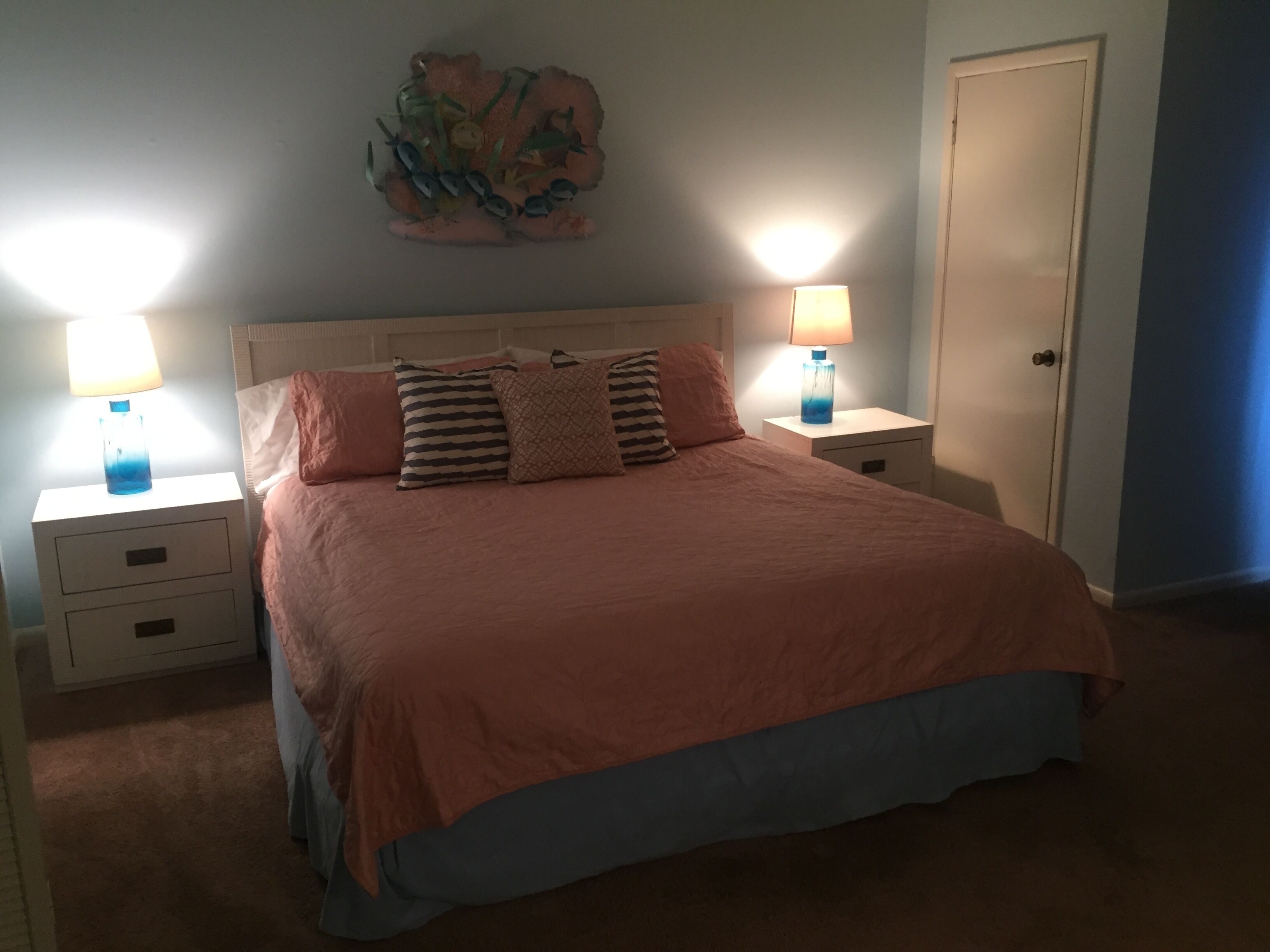 Un letto rifatto con cura, con copriletto color pesca e diversi cuscini, affiancato da due comodini con lampade.