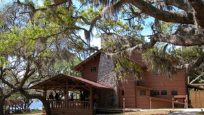 A rustic cabin with a porch, surrounded by large trees and a clear sky.