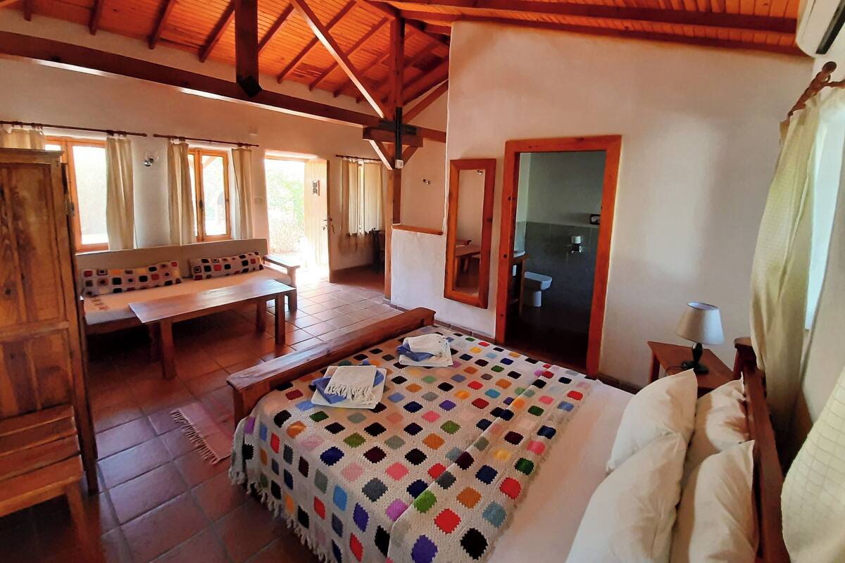 Una habitación acogedora con techo de madera, una cama con una manta colorida, un banco y una pequeña mesa.