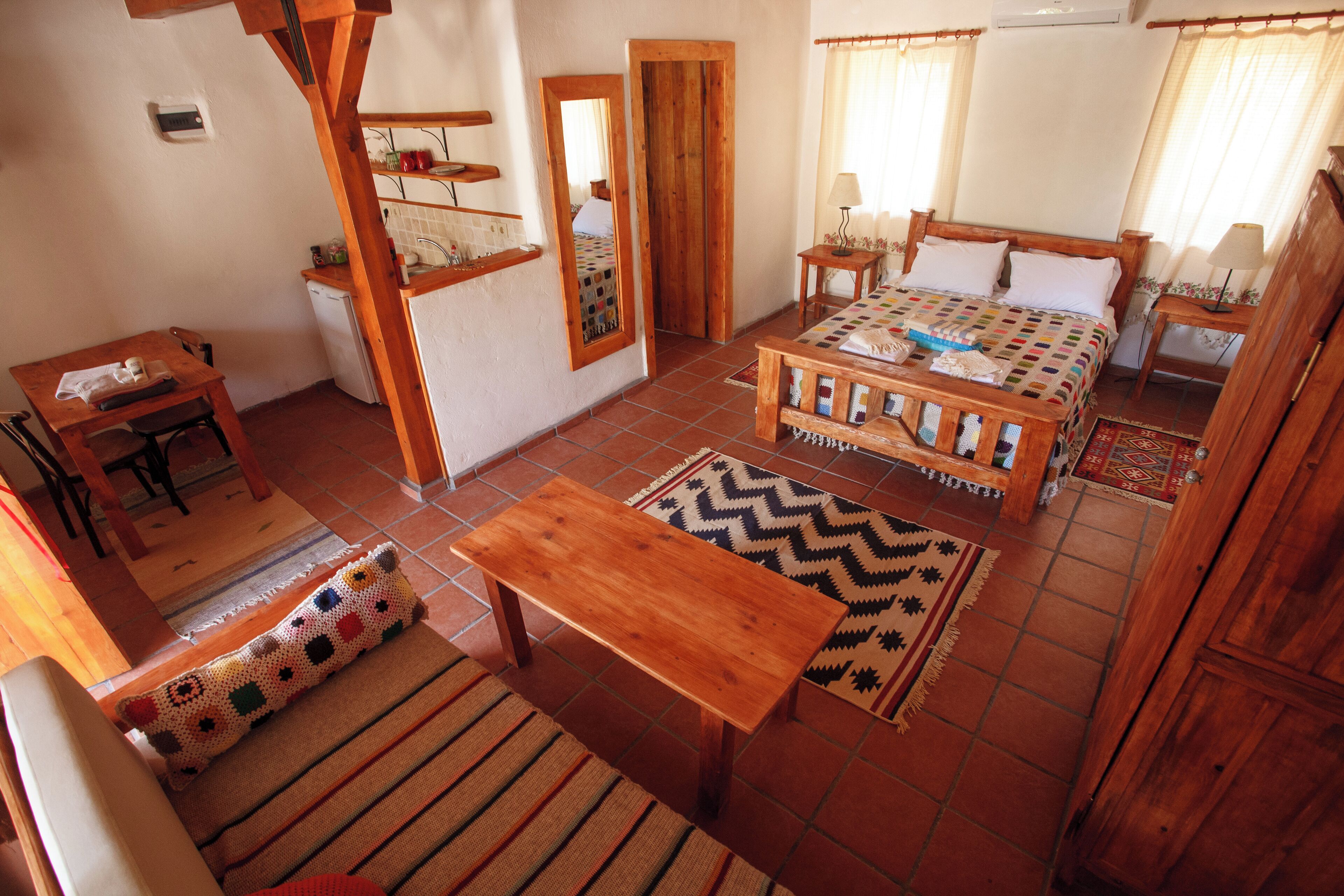 Um quarto aconchegante com uma cama, uma escrivaninha de madeira, uma cadeira, uma mesinha e um espelho.