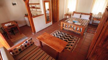 Um quarto aconchegante com uma cama, uma escrivaninha de madeira, uma cadeira, uma mesinha e um espelho.