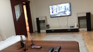 A hotel room with a TV mounted on the wall, a wooden coffee table with wine glasses and a chocolate bar, and two remote controls. - Apartman Sever Hroncova (Kosice)