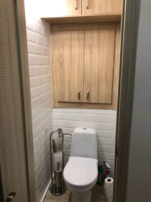 Ein kleines Badezimmer mit einer weißen Toilette, einem Holzschrank darüber und einer Toilettenbürste.