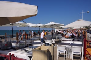 An outdoor dining area with tables and chairs under umbrellas, overlooking a body of water. - "Le Cardinal" Fécamp Seaside in Normandy 76 (Fécamp)