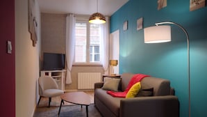 Ein Wohnzimmer mit einer Couch, einem Sessel, einem Tisch, einer Stehlampe und einem Fernseher.