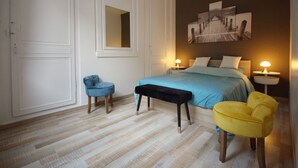 Ein Schlafzimmer mit Bett, Nachttischen, einem Sessel, einer Bank und einem großen Gemälde an der Wand.