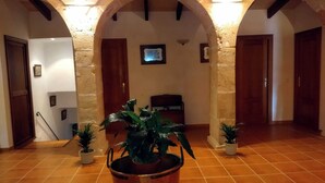 A hallway with tiled flooring, wooden doors, and a large potted plant in the center. - Cottage in the middle of nature (Petra)