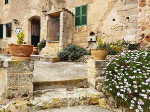 Un bâtiment en pierre avec une entrée rustique, des marches menant à une porte et des plantes en pot.