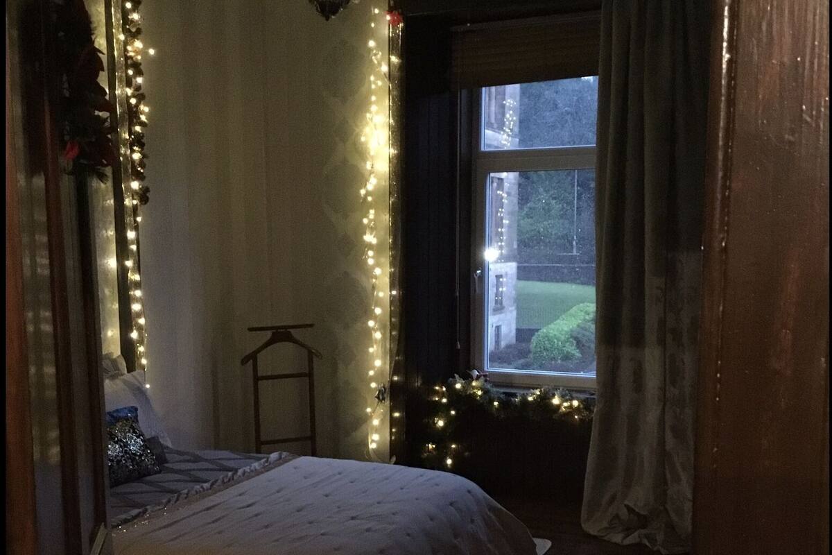 Ein Schlafzimmer mit Bett, einem Fenster mit Vorhängen und Lichterkette.