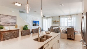 A modern kitchen with a central island, built-in appliances, and a dining area with a view of the living room. - Ideal Retreat Townhome Oasis with Pool - 4801 ML (Kissimmee)