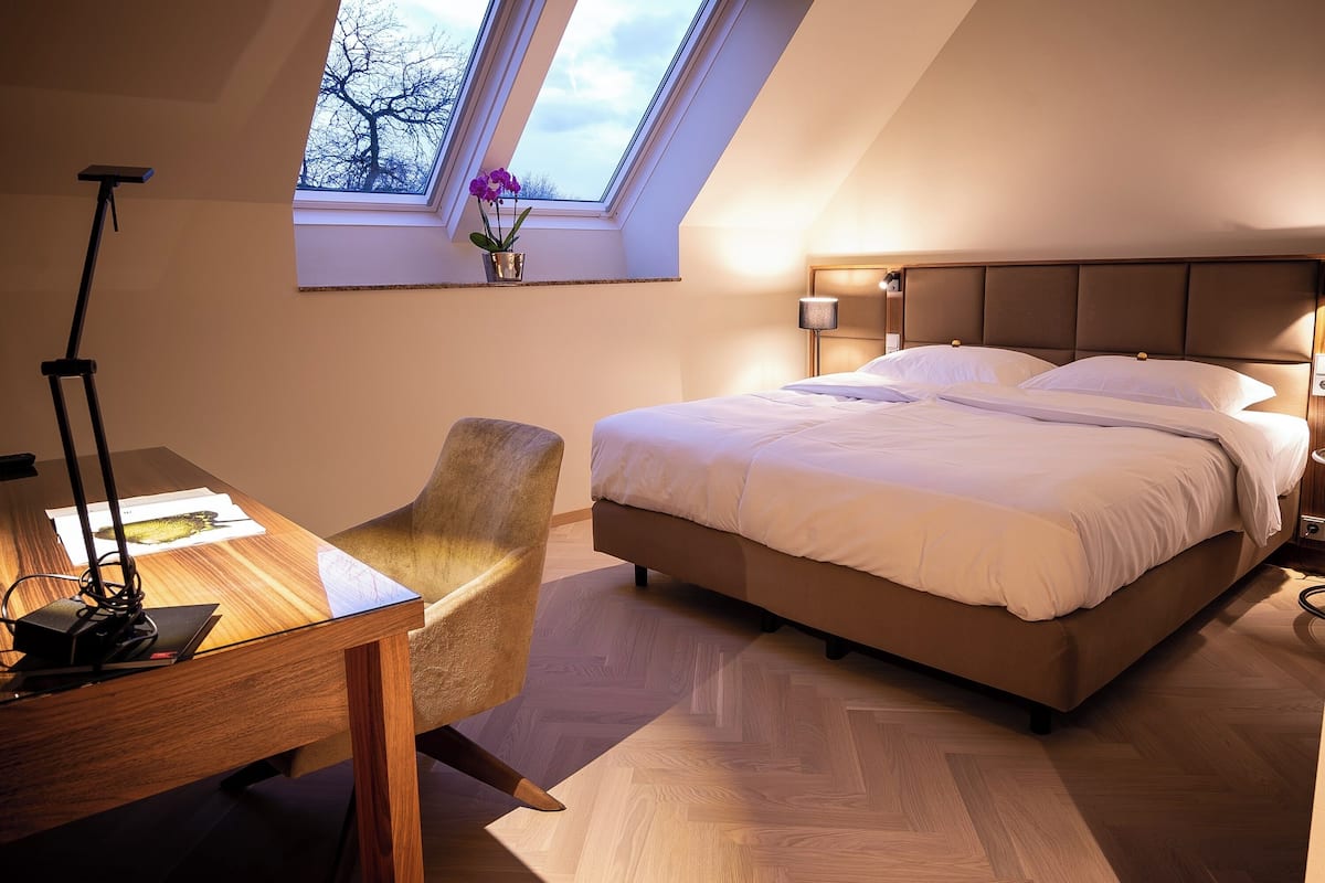 Une chambre avec un grand lit, un bureau avec une lampe, une chaise et une lucarne.