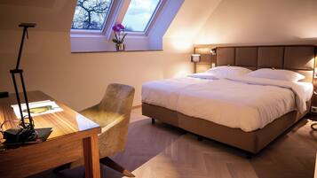 A bedroom with a large bed, a desk with a lamp, a chair, and a skylight.