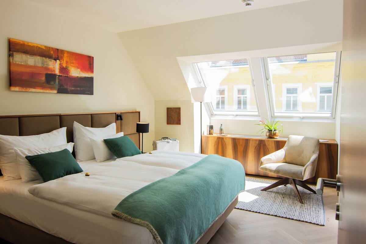 Une chambre d’hôtel avec un grand lit, un bureau, une chaise, une fenêtre et un tableau au mur.