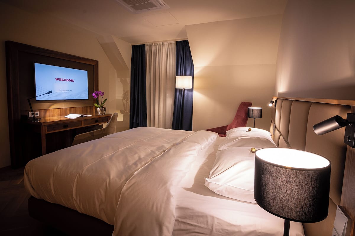 Une chambre d’hôtel avec un lit, un bureau, un téléviseur affichant le mot « BIENVENUE », une lampe et une fenêtre avec des rideaux.