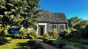 A house with a brick pathway leading to the front door, surrounded by well-maintained gardens and trees. - Cute, Quiet, Comfortable, Centrally Located, Outdoor Shower, Large Yard, BBQ (Nantucket)