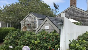 A traditional wooden house with a gabled roof, surrounded by lush greenery and a white picket fence. - Cute, Quiet, Comfortable, Centrally Located, Outdoor Shower, Large Yard, BBQ (Nantucket)