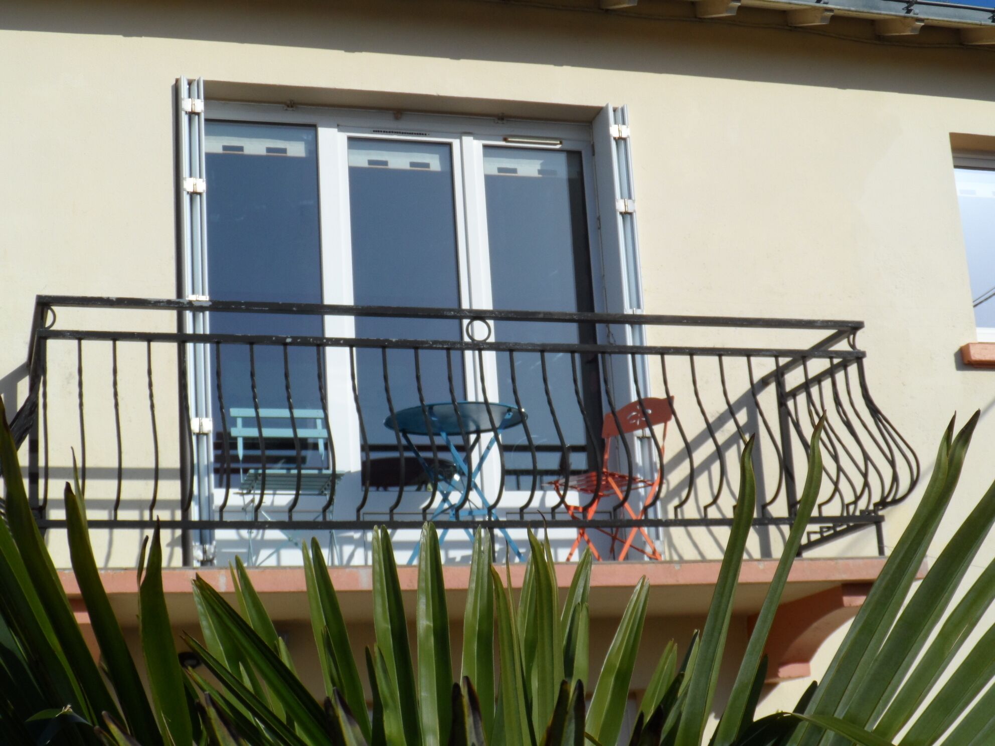 Ein Balkon mit Metallgeländer, einem Tisch und zwei Stühlen.
