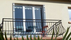 Een balkon met een metalen hekwerk, een tafel en twee stoelen.