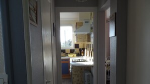 Een smalle gang die uitkomt in een keuken met een raam, kastjes en een koelkast.