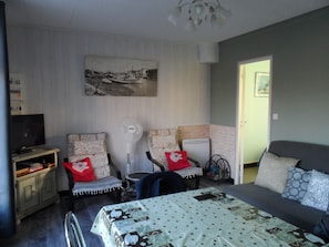 Une chambre à coucher avec un lit, deux chaises, une télévision, un ventilateur et un tableau accroché au mur.