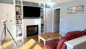 Un salon avec une cheminée, des étagères à livres, un téléviseur et un canapé en cuir rouge.