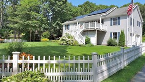 Une maison à deux étages avec une clôture en bois peinte en blanc, des panneaux solaires et une pelouse bien entretenue.