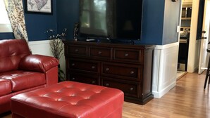A living room with a red leather sofa, a television on a wooden cabinet, and a map on the wall. - Swamp Rabbit Retreat (Travelers Rest)