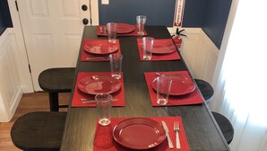 A dining table set with red placemats, plates, and glasses, surrounded by black chairs and a bench. - Swamp Rabbit Retreat (Travelers Rest)