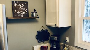 A kitchen with a marble countertop, white cabinets, a coffee maker, and a sign that reads "Wine A Little Laugh A Lot". - Swamp Rabbit Retreat (Travelers Rest)