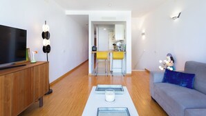 A modern living room with a flat-screen TV, a wooden cabinet, a sofa, and a kitchen area in the background. - Home2Book Design Santa Úrsula Pool & Wifi (Sta Úrsula)