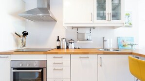A modern kitchen with white cabinetry, a stainless steel range hood, a built-in oven, a coffee maker, and a yellow chair. - Home2Book Design Santa Úrsula Pool & Wifi (Sta Úrsula)