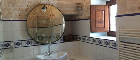 A bathroom with a white sink, a round mirror, and a window with a wooden door.