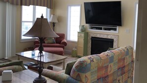 A living room with a sofa, a television, a fireplace, and a ceiling fan. - I LOVE BEACH MUSIC (Ocean Isle Beach)