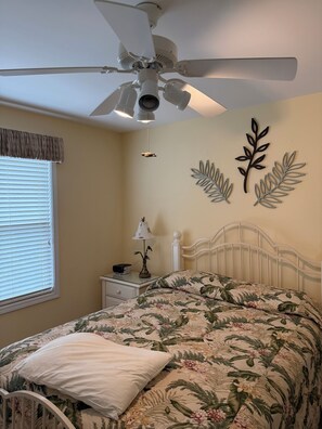 Ein Schlafzimmer mit Bett, Deckenventilator, Nachttisch mit Lampe und Wandbildern.