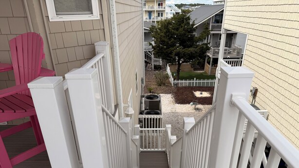 A wooden staircase with white railings leading to a balcony with a pink chair. - I LOVE BEACH MUSIC (Ocean Isle Beach)
