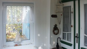 A cozy room with a bench, a door with green trim, a window with a sailboat model, and a rug with a lighthouse design.