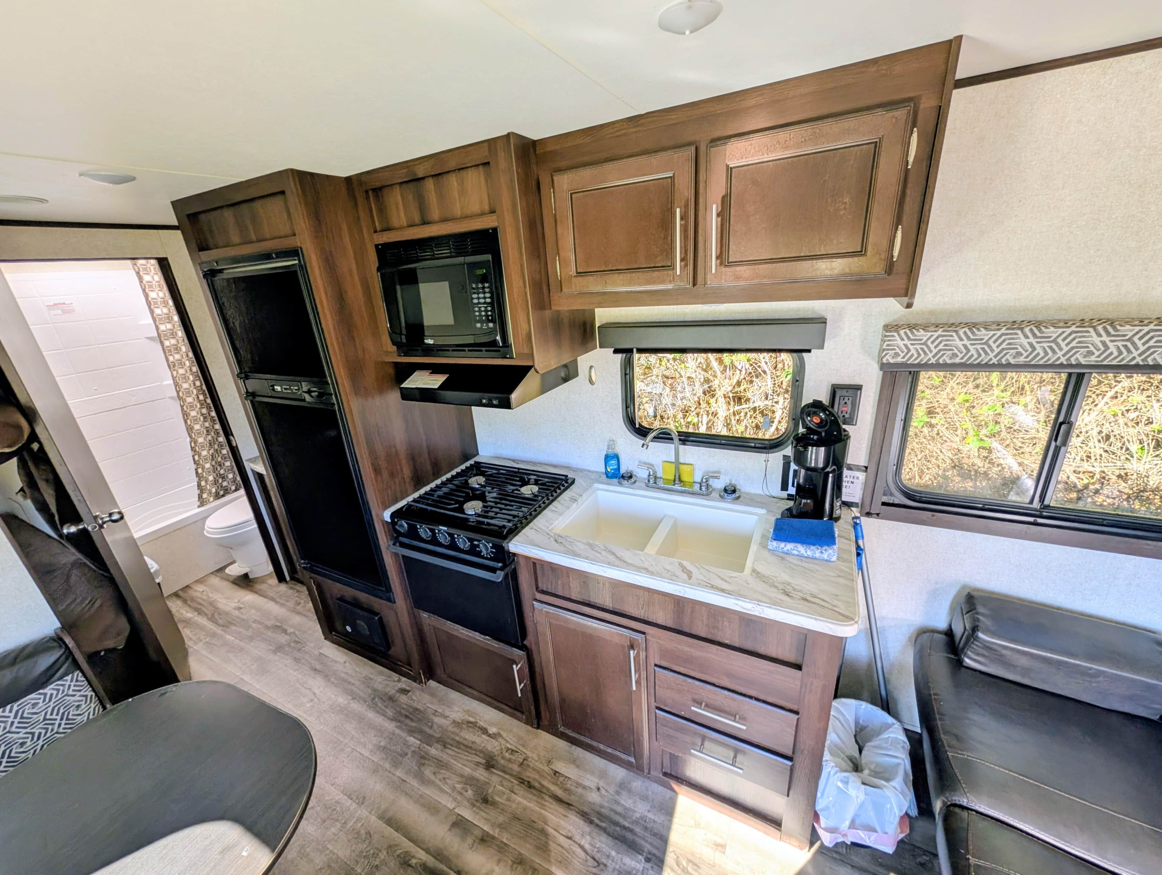 A compact RV kitchen with a stove, microwave, and sink.
