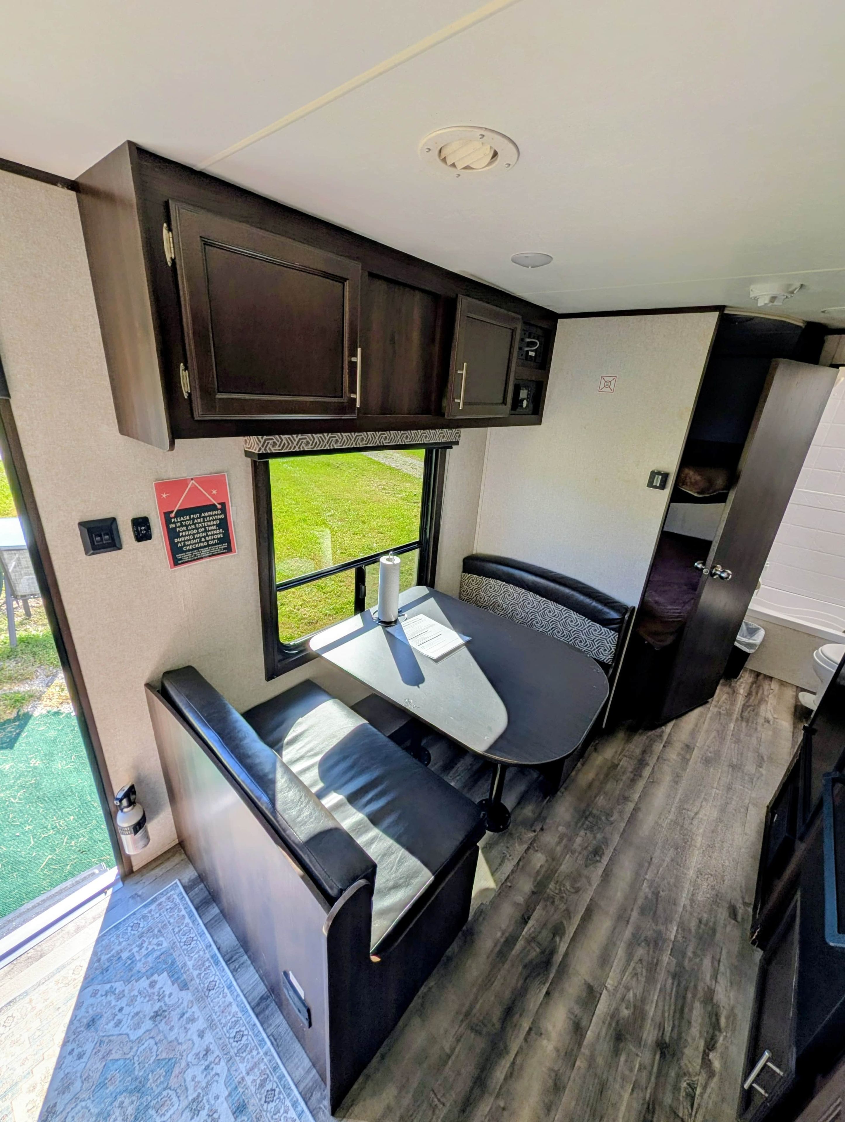 A compact RV interior with a kitchenette, a dining area, and a small window offering a view.