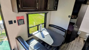 A compact RV interior with a kitchenette, a dining area, and a small window offering a view.
