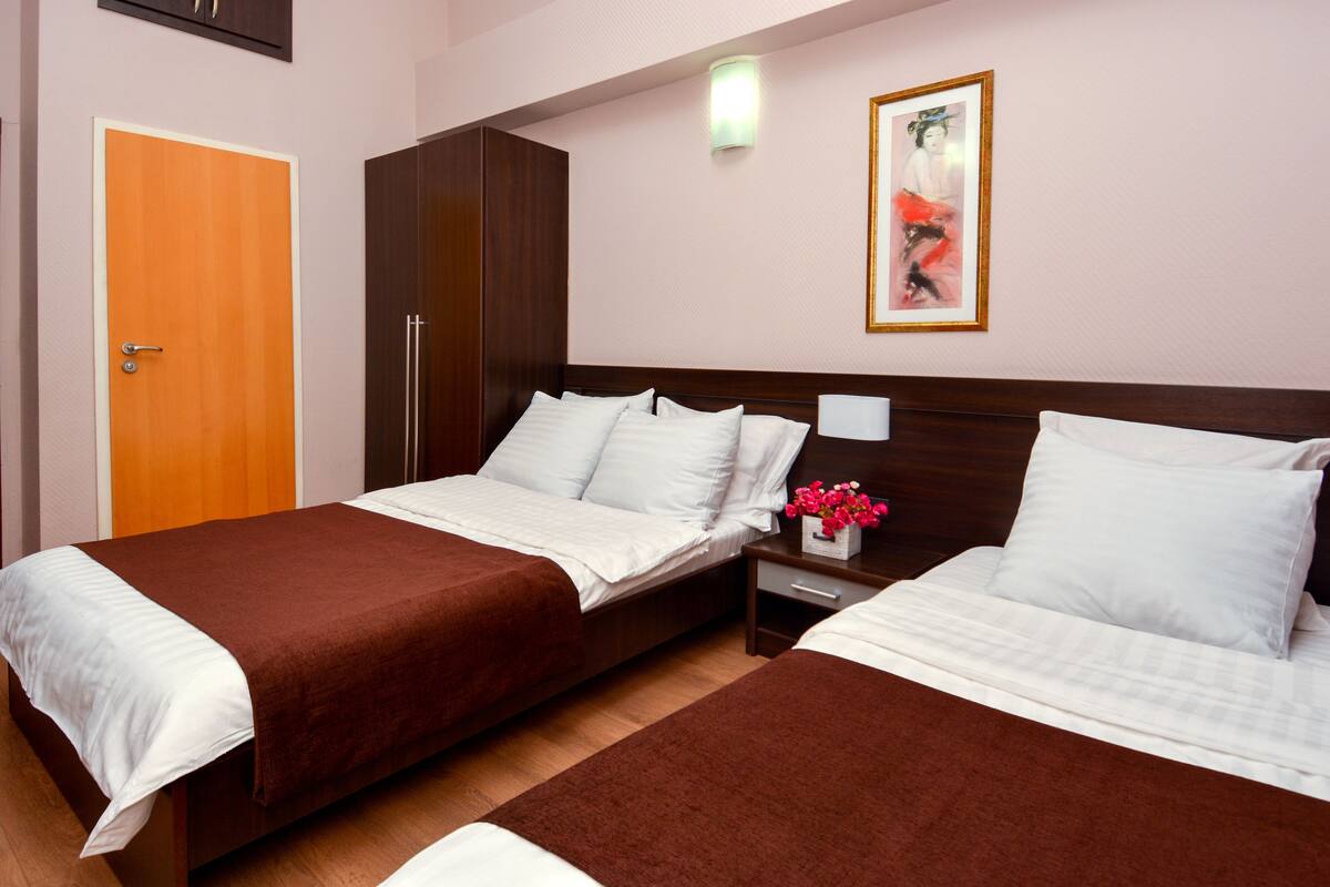 Habitación de hotel con dos camas, un armario, una mesita de noche con lámpara y un cuadro en la pared.