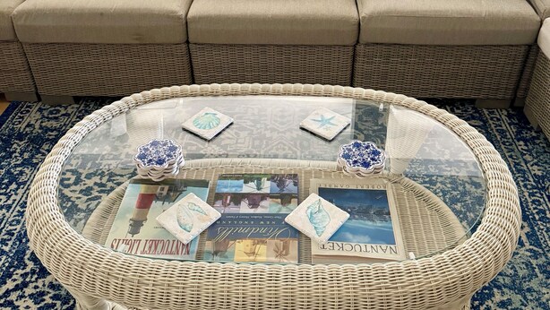 Una sala de estar con una mesa de centro de mimbre, un tapete estampado y un sofá con cojines decorativos.