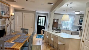 Una cocina moderna con una isla central, muebles blancos y un comedor con mesa y sillas de madera.