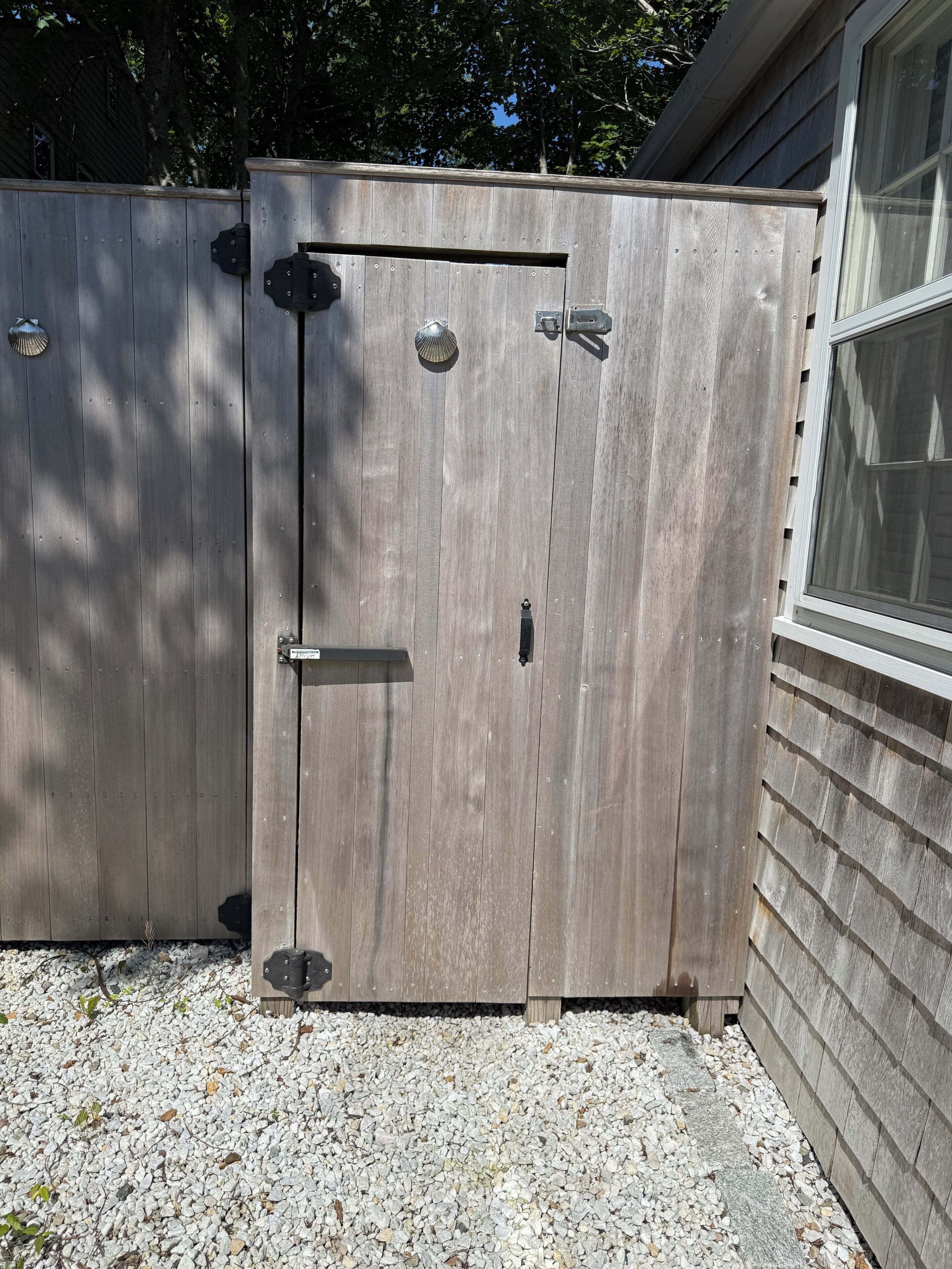 Een houten tuinhuis met een metalen grendel en een klein plankje.