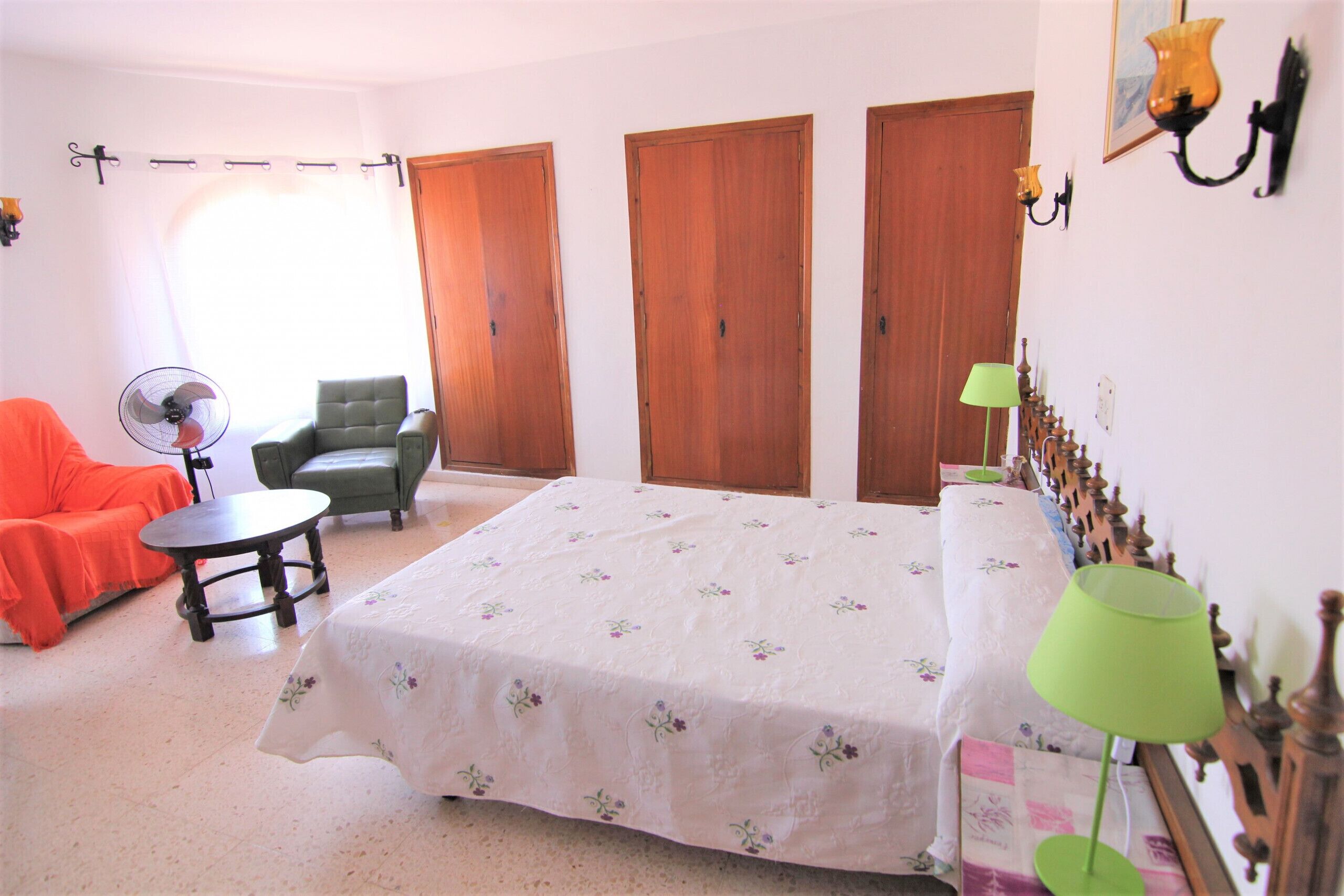 A bedroom with a bed, a chair, a table, and a lamp.