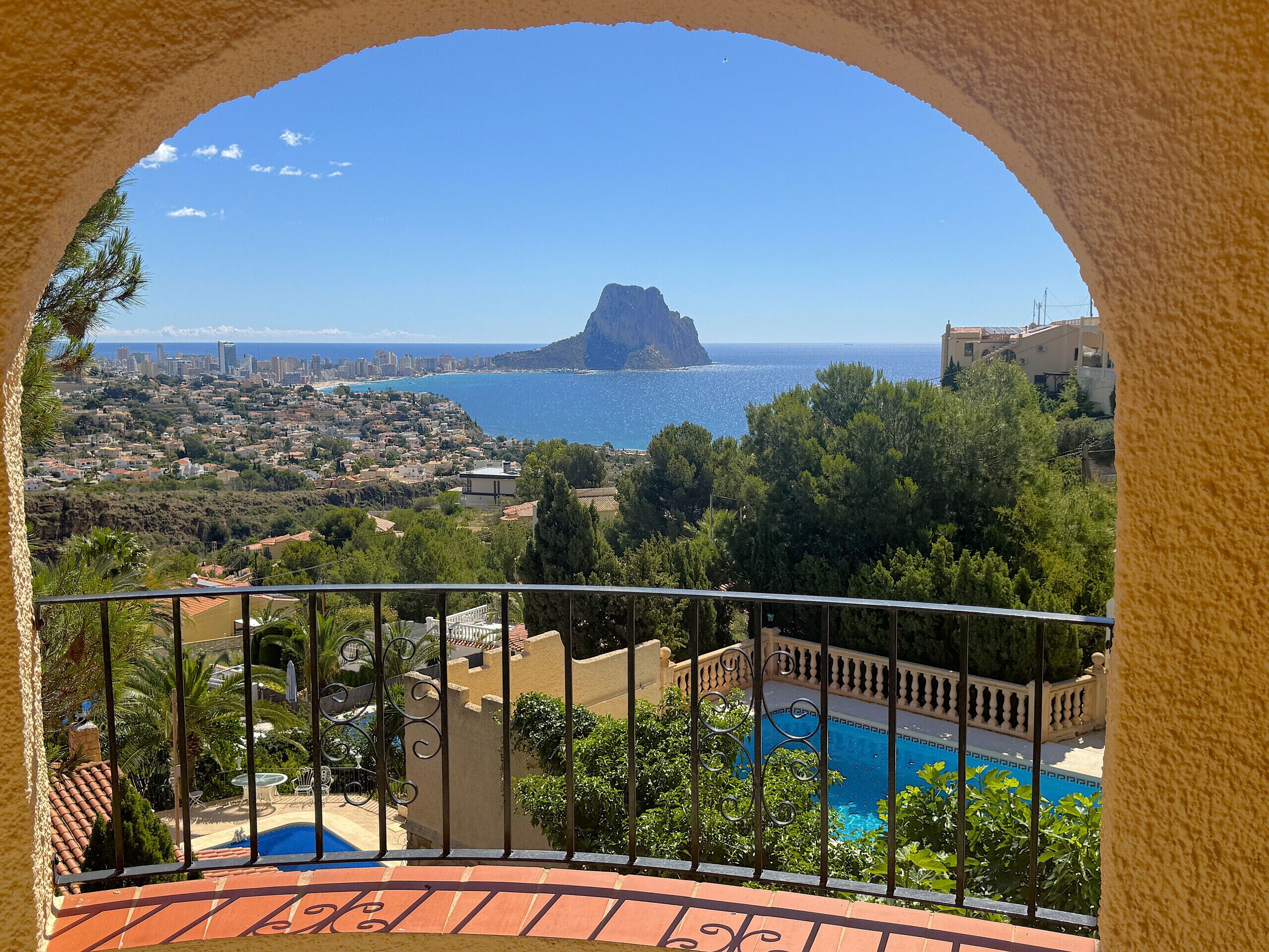 Ein Balkon mit Blick auf eine Küstenstadt, einen Berg und ein Schwimmbad.