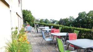 An outdoor patio with multiple tables and chairs, surrounded by greenery and a hedge. - Lovely home in Auerbach with sauna (Auerbach)