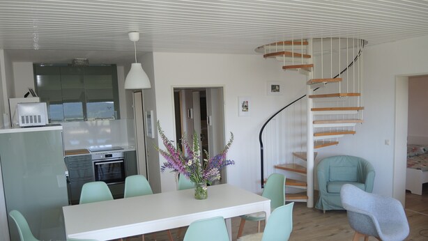 A modern kitchen with a built-in oven and microwave, a dining area with a white table and light green chairs, and a spiral staircase leading to an upper level. - Renovated, bright, light-flooded 4-room apartment (Saig)