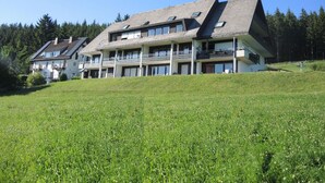 A multi-story hotel with balconies, set on a grassy hill with a forest in the background. - Renovated, bright, light-flooded 4-room apartment (Saig)